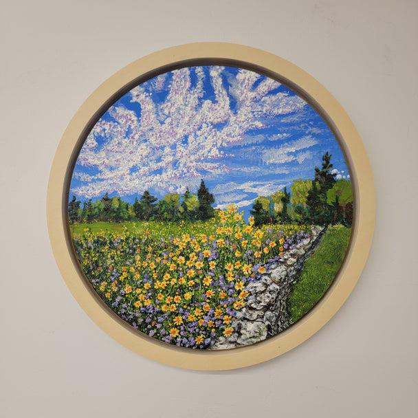 Round Framed Painting depicting a stone wall ush flower meadow and textural clouds in the sky.