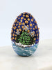 Decorative hand painted egg with trees on an island and gold stars in a night's sky
